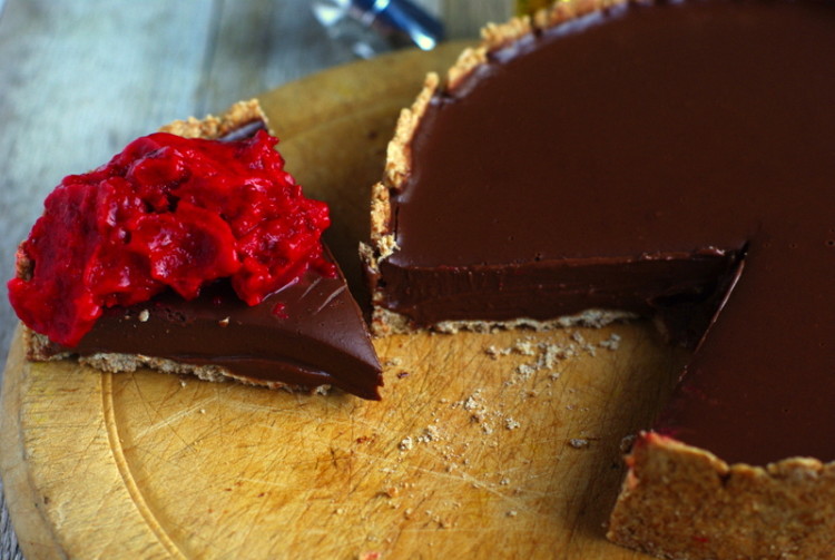 A rustic, straight sided tart filled with glossy chocolate filling and topped with a dollop or shiny red sorbet.
