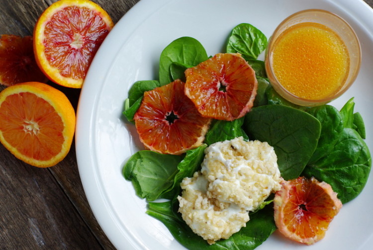 Glossy green spinach leaves topped with two discs of oozy nut crusted goat's cheese and slices of blood orange.