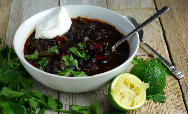 Bowl of black soup filled with glossy black beans, shreds of red pepper and topped with fresh green coriander leaves and a dollop of yogurt.