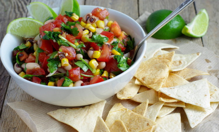 A vibrant, colourful bowl of fresh salsa with black eyed beans throughout and baked tortilla chips.